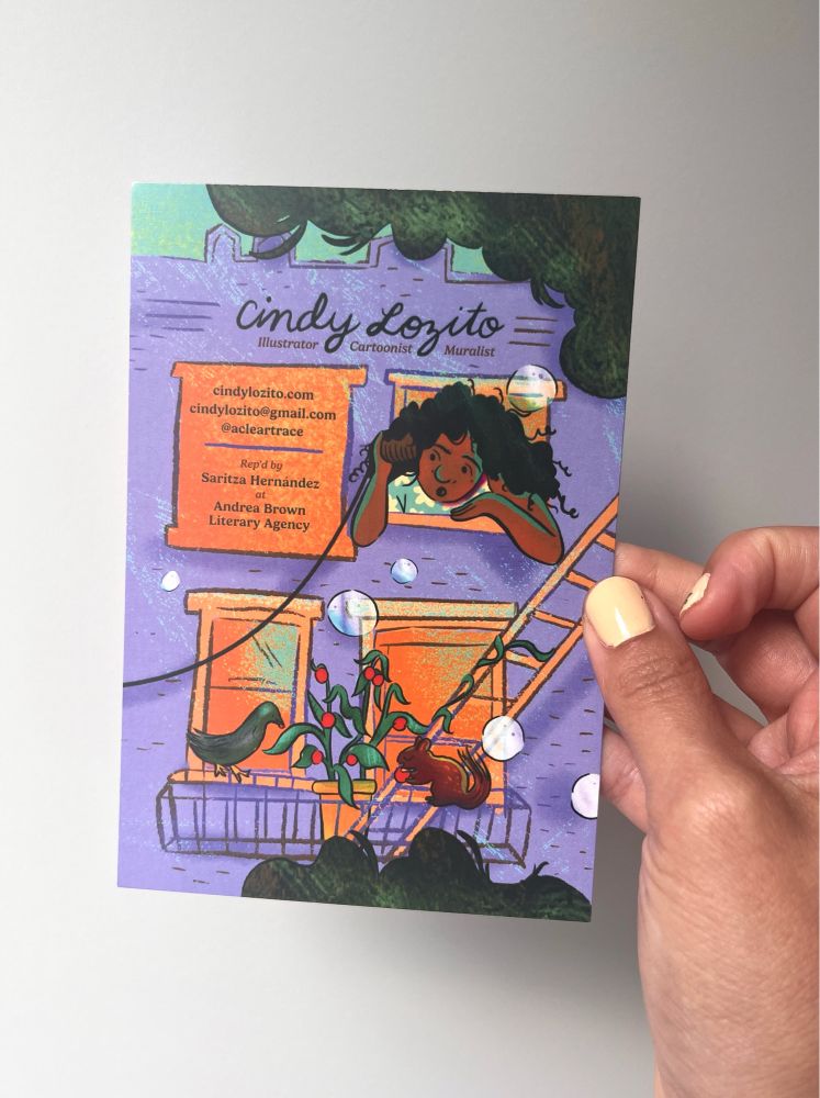 Cindy Lozito’s hand holds up one side of a kid lit art post she made showing a girl playing telephone with a can and string, and a pigeon and squirrel feasting on a fire escape plant.