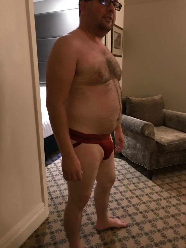 Naked guy wearing a red jock strap and smirking