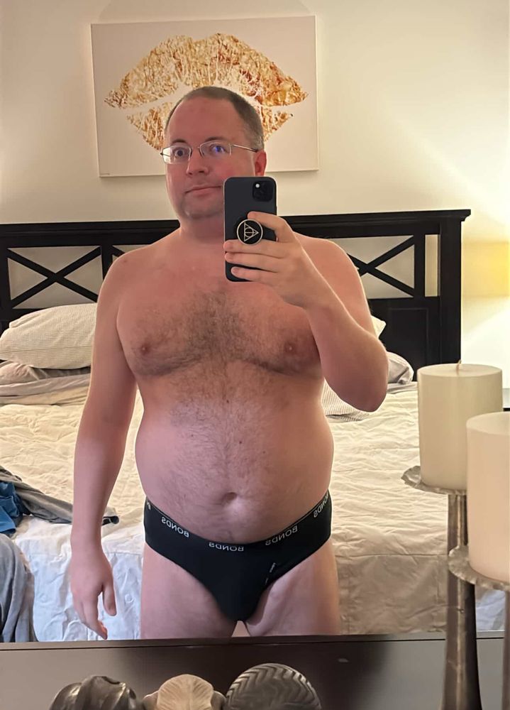 Half naked furry guy standing in front of a mirror in black briefs