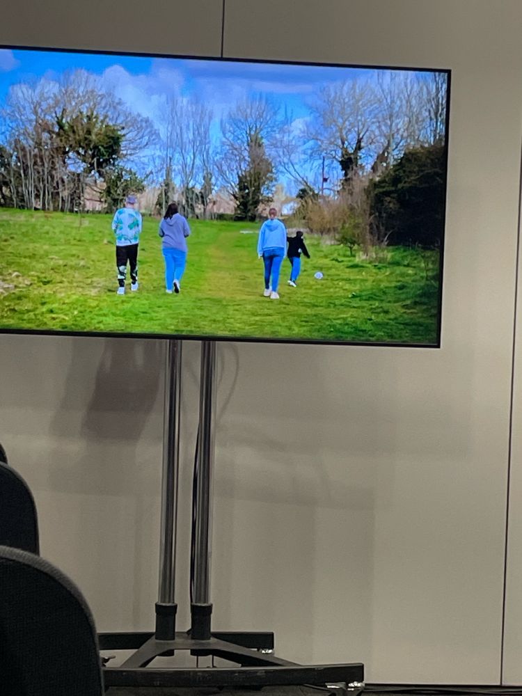 A still from the stroke association film showing a stroke survivor, his partner and two children from the back as they walk across a grassy space. This is shown on a television screen.
