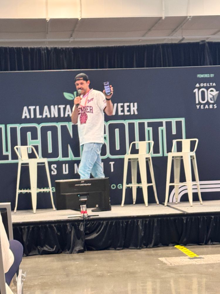 A man walking on stage on a microphone holding up his phone