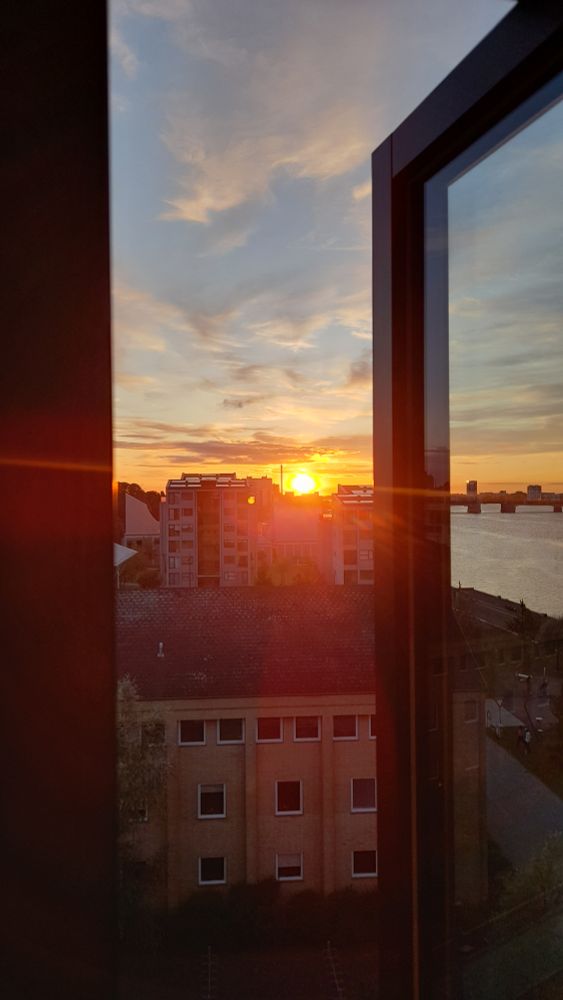 The sun sets, as can be seen through a window on uni campus. The shore can be seen on the right hand side.