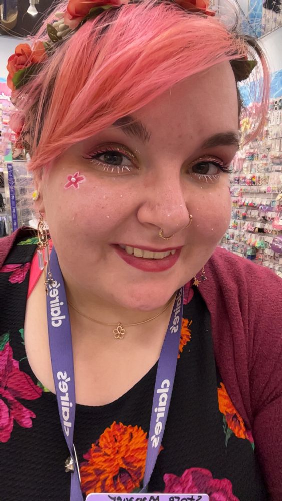 Pink hair girl with nose rings. She has flowers on her shirt, in her hair, and as makeup on her face 