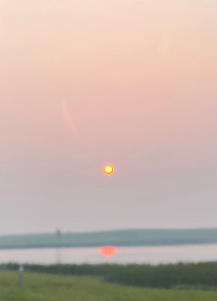 Hazy sun in sky and also reflecting over water.
