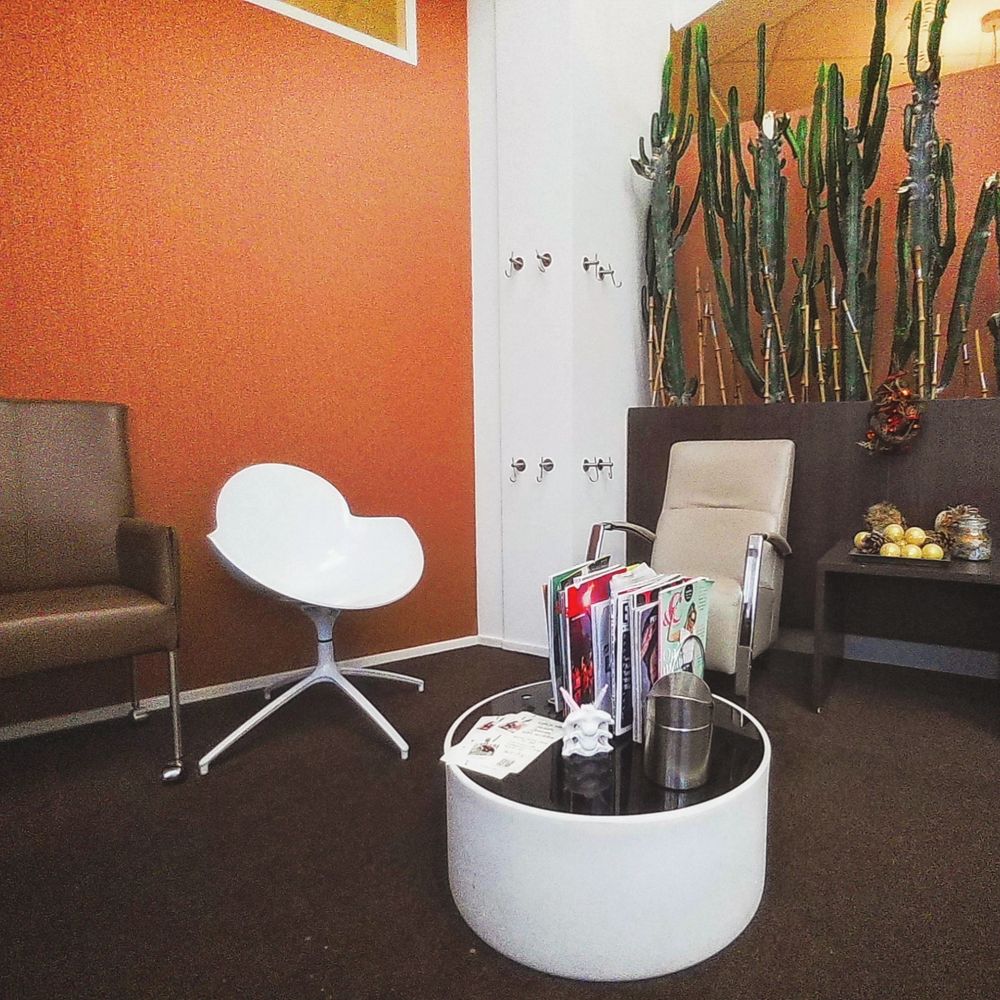 A waiting room with chairs and magazines on a table in the middle, the walls are orange colour.
