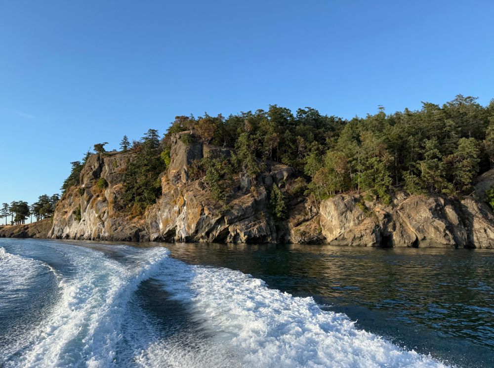 An island cliff is sunset lighting with a boat wake trailing in front of it 