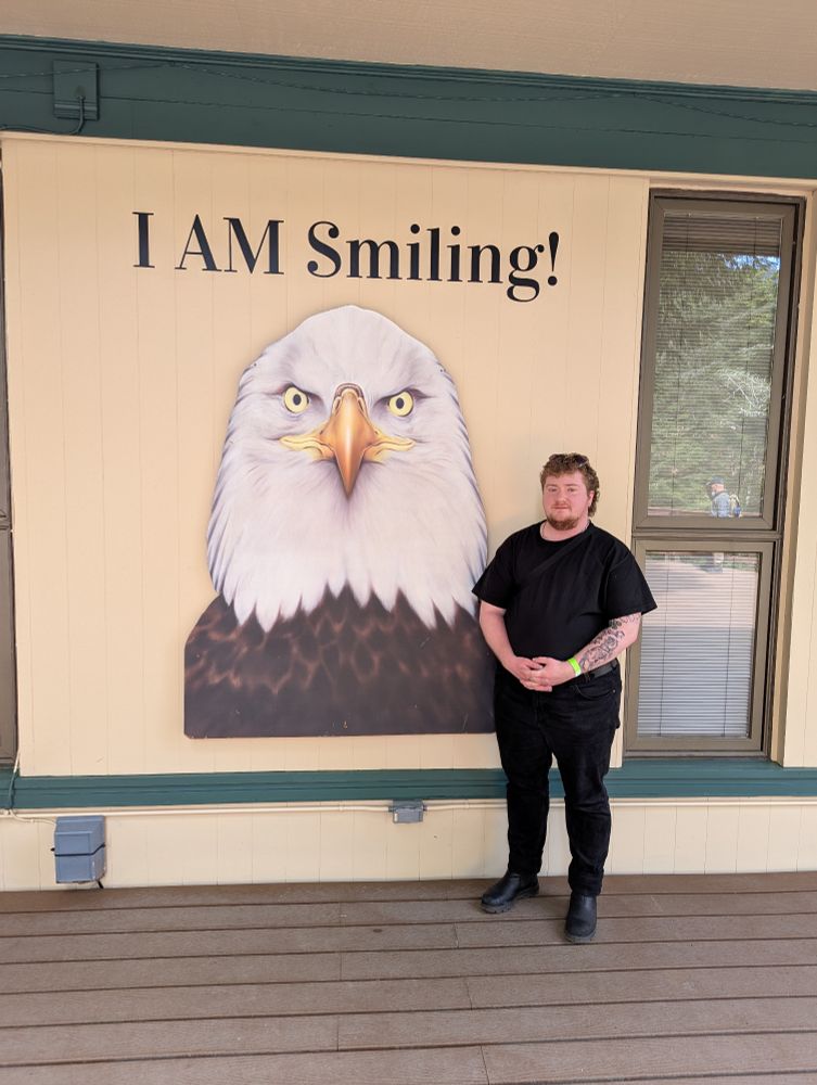 Photo of my fiance standing in front of a large graphic of an eagle captioned 