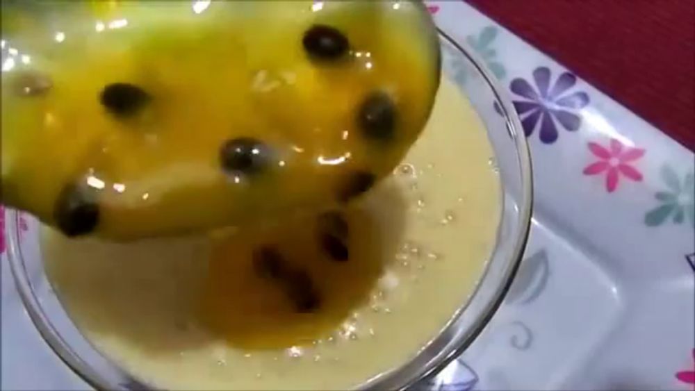 a spoon is pouring a yellow liquid into a glass on a plate with flowers on it