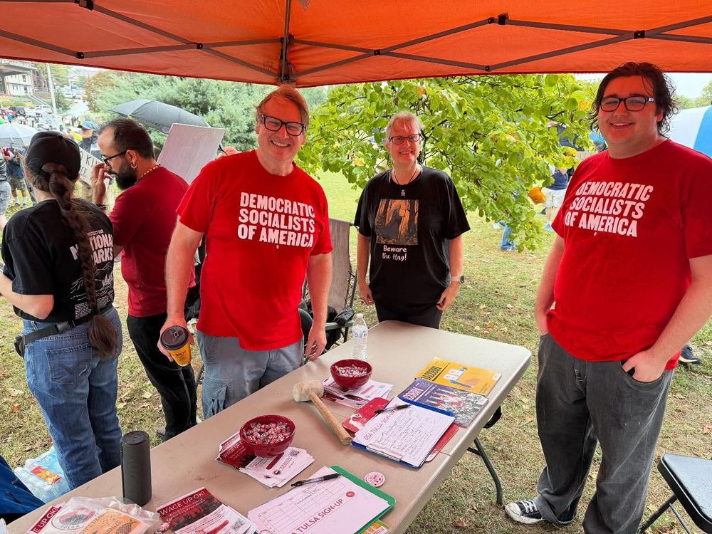 Four people are standing next to a table at a No Kings rally. 