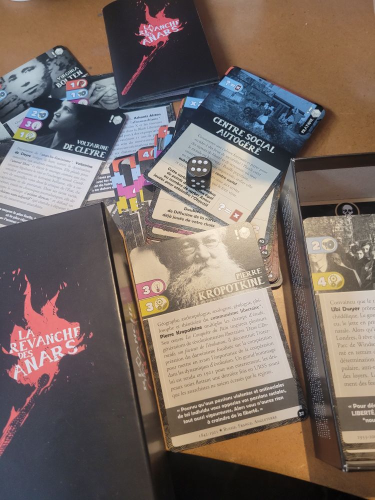 Jeu La Revanche des anars ouvert. On y voit des cartes à jouer, un dé  un livret de règles.