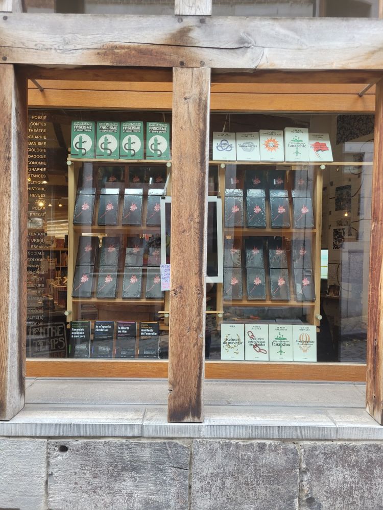 Photo de la vitrine de la librairie Entre-Temps exposant de nombreux exemplaires du jeu de société La Revanche des Anars. Un jeu édité par l'asbl Barricade.