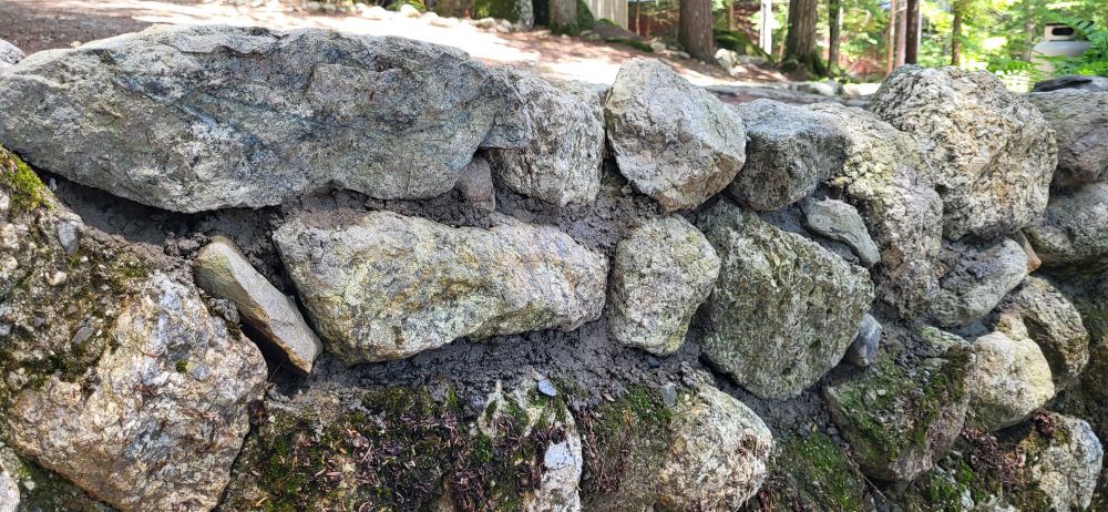 Rock retaining wall, with rebuilt upper section at a family camp in Maine. Lower portion has moss (indicating it's age) upper, new section has wet concrete between various stones placed by the author of this post