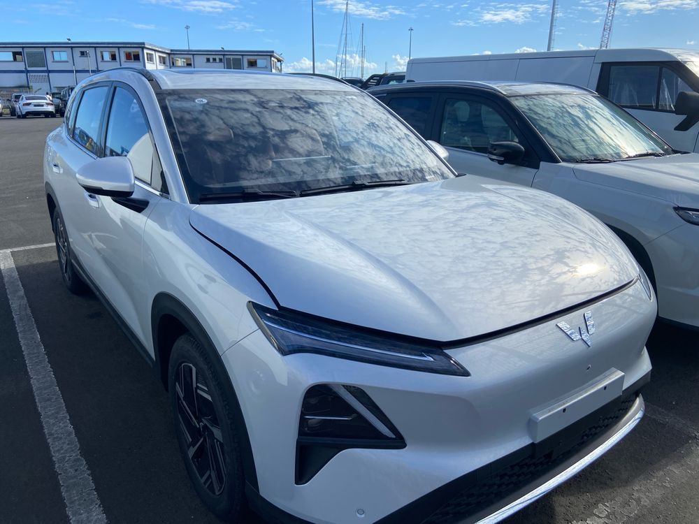 A silver SUV sits in a parking lot among many other cars waiting for transportation to a car lot.