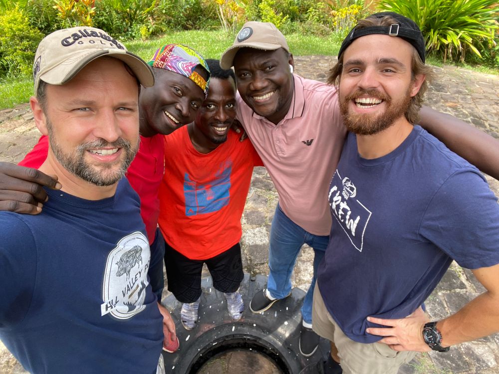 Five men, two white and three black, are taking a selfie standing on a tractor tire.