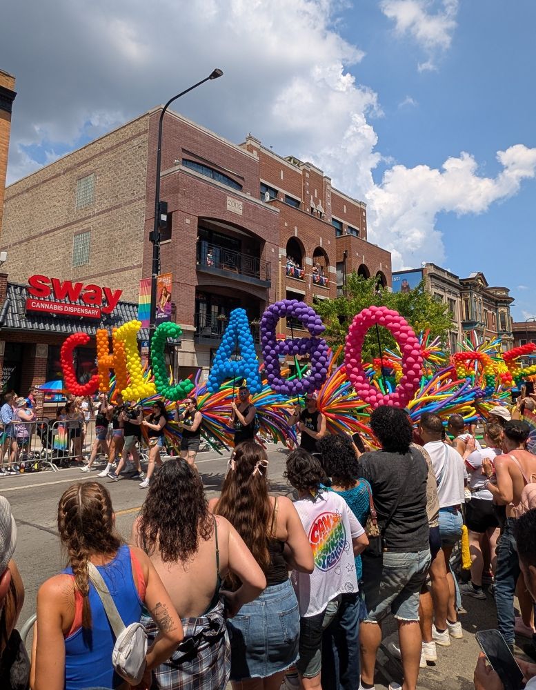 Chicago Pride Parade, with people holding balloons forming the word "Chicago" out of a rainbow of colors