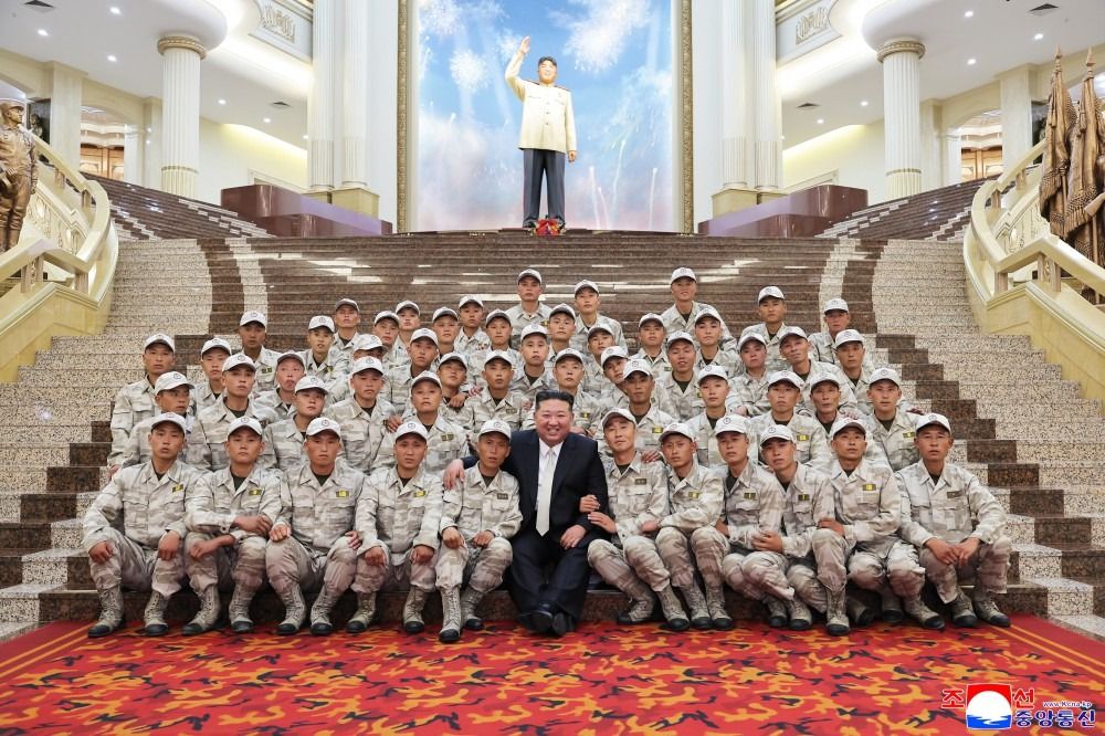 Kim Jong Un sitting with dozens of troops in camouflage wear in the Victory Museum.
