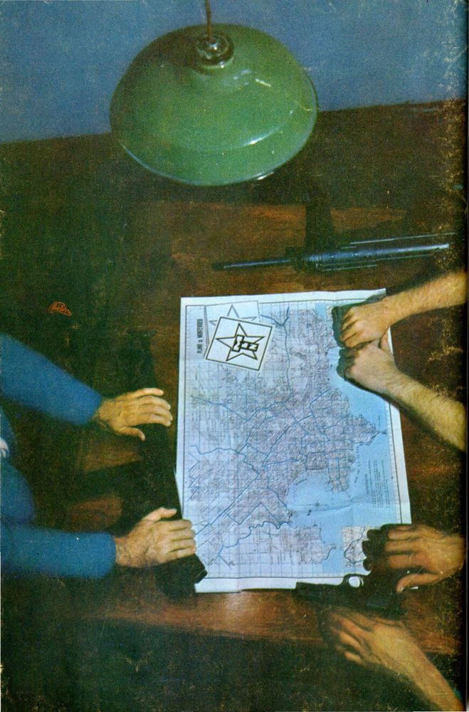 A contracapa são mãos colocando armas sobre uma mesa em que há um mapa. Sobre a mesa há uma luminária verde. 