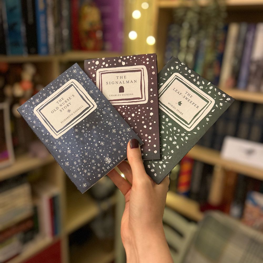 Three short story books held in a fan shape in front of bookcases