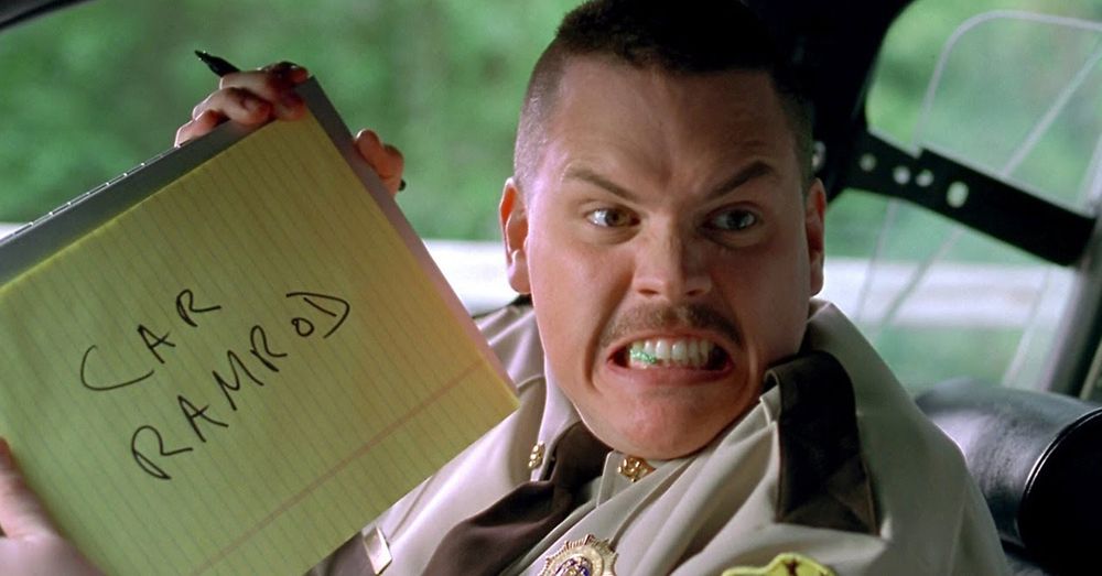 Super troopers reference. cop in passenger seat seething with a yellow notepad that says “team ramrod” 
