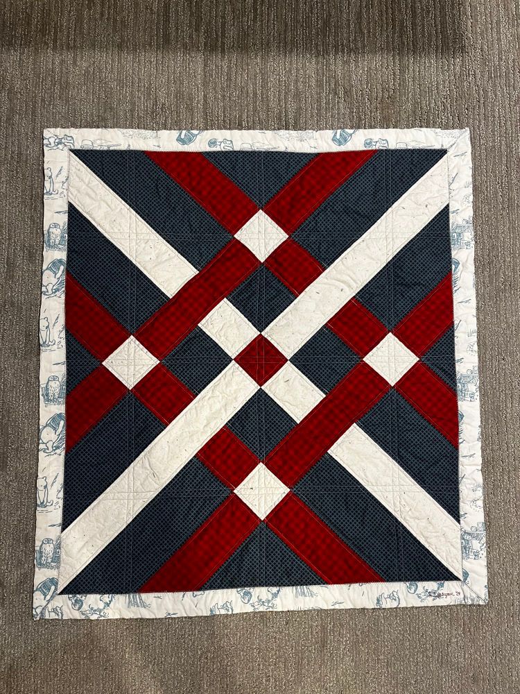 A fishing net pattern baby quilt with a navy background and a crimson and white pattern on top.