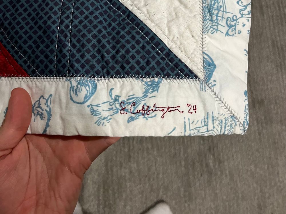 A close up on my embroidered signature in red on the lower right hand corner of the quilt