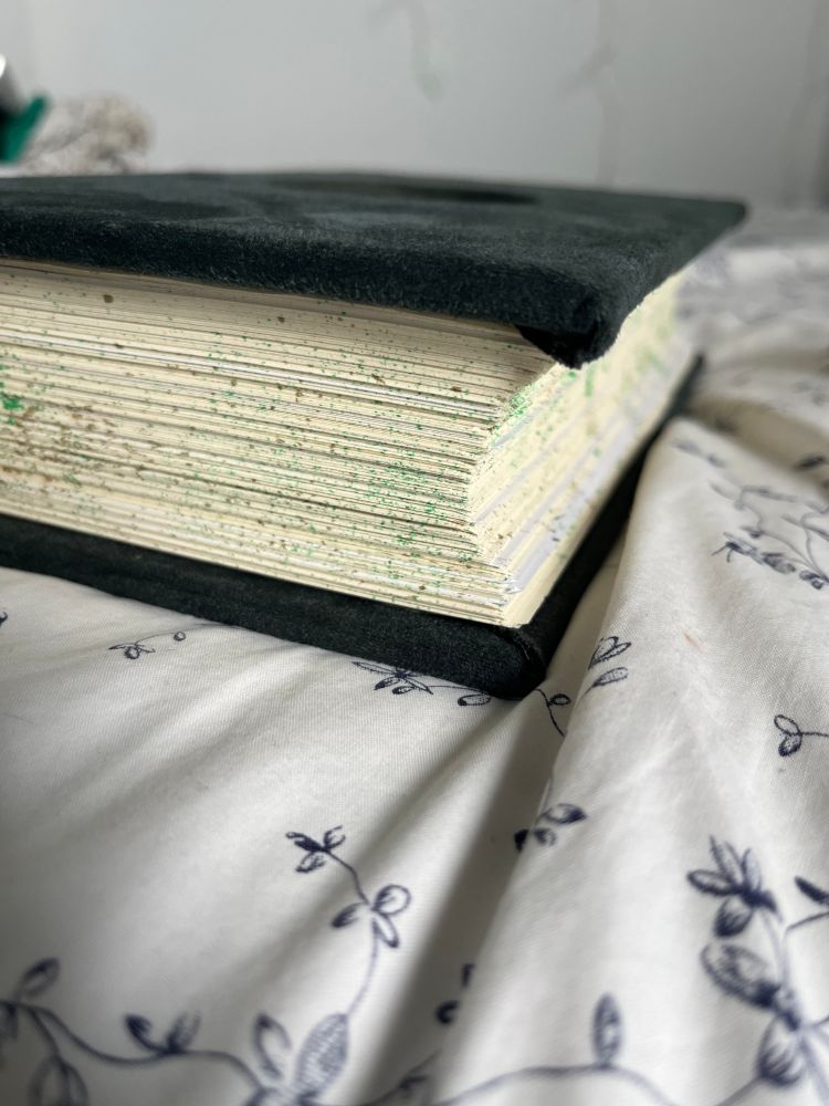 the side of the same green velvet book, focusing on the inward curve of the cream and speckled pages
