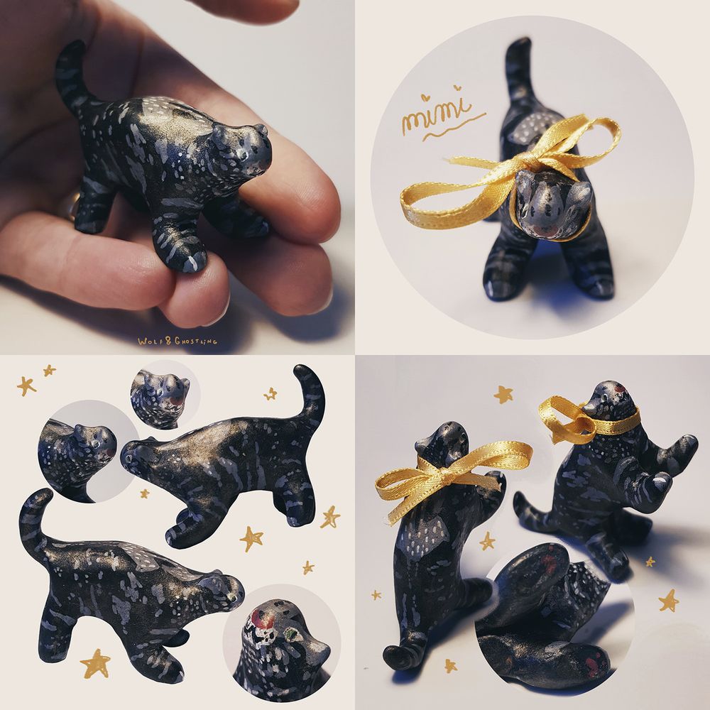 photos of a very tiny cat sculpture. she is black with grey patterning and a cute little face. she wears a silky yellow ribbon around her neck.