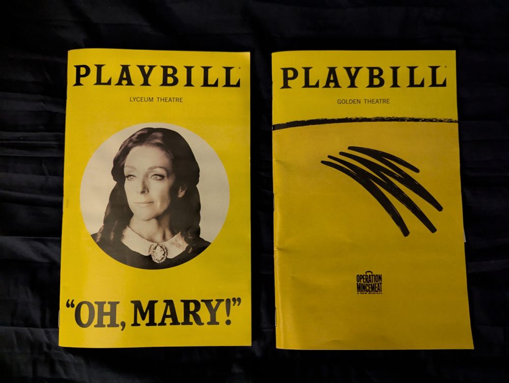 Two predominantly yellow playbills sitting on a bed. "Oh, Mary!" & "Operation Mincemeat"