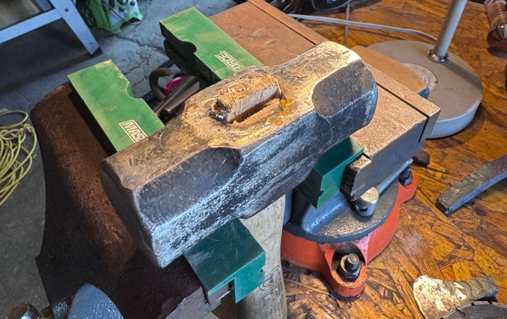 3# sledge hammer held in a bench vise. The center of the wedge in the eye is jutting up and showing a gap between the empire if the end of the handle. 