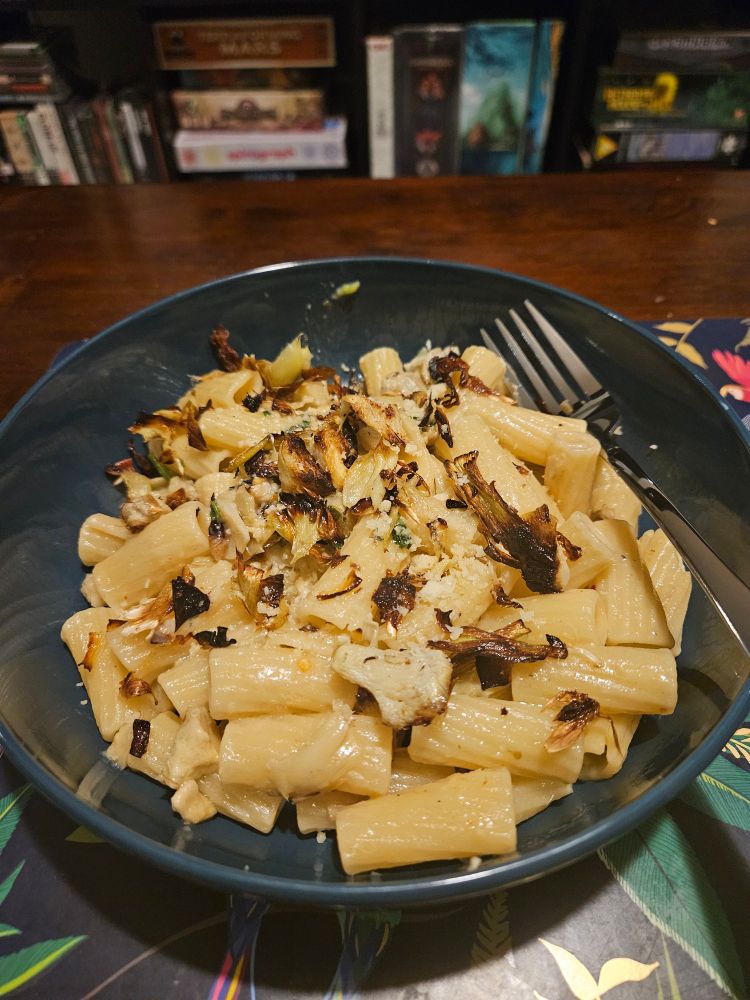 A concoction of rigatoni noodles, crisped artichoke hearts, and melted Parmesan in a blue bowl.