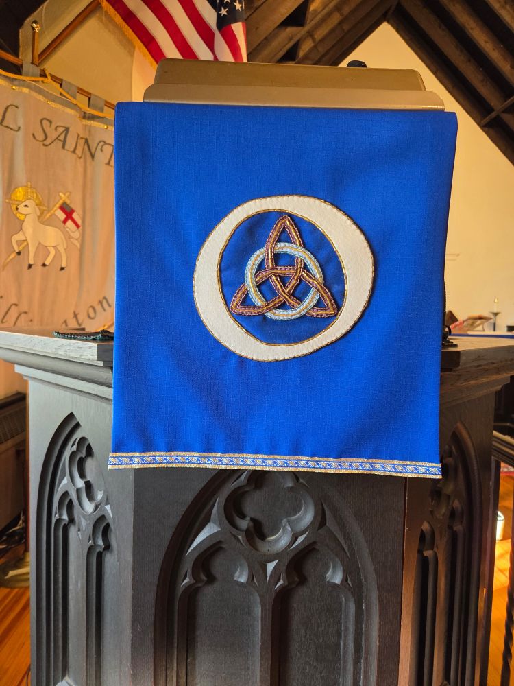 Blue pulpit fall with a Trinity knot inside a white "O".   
