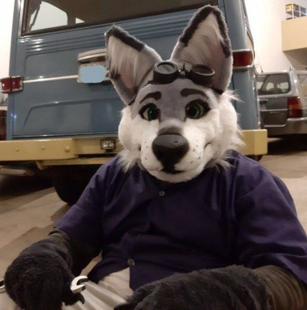 Luke is sitting behind a car holding a wrench 