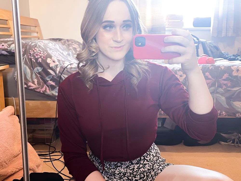 picture of me sitting on the floor taking a selfie, clothed in a red crop hoodie and black/white flowery shorts