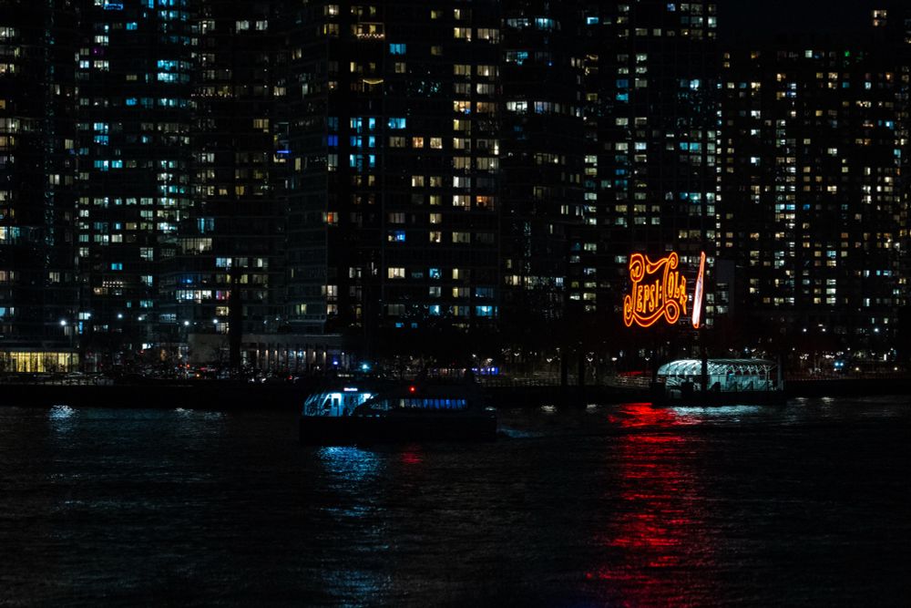 Pepsi cola picture with boat passing in front of it taken from Roosevelt island in NYC