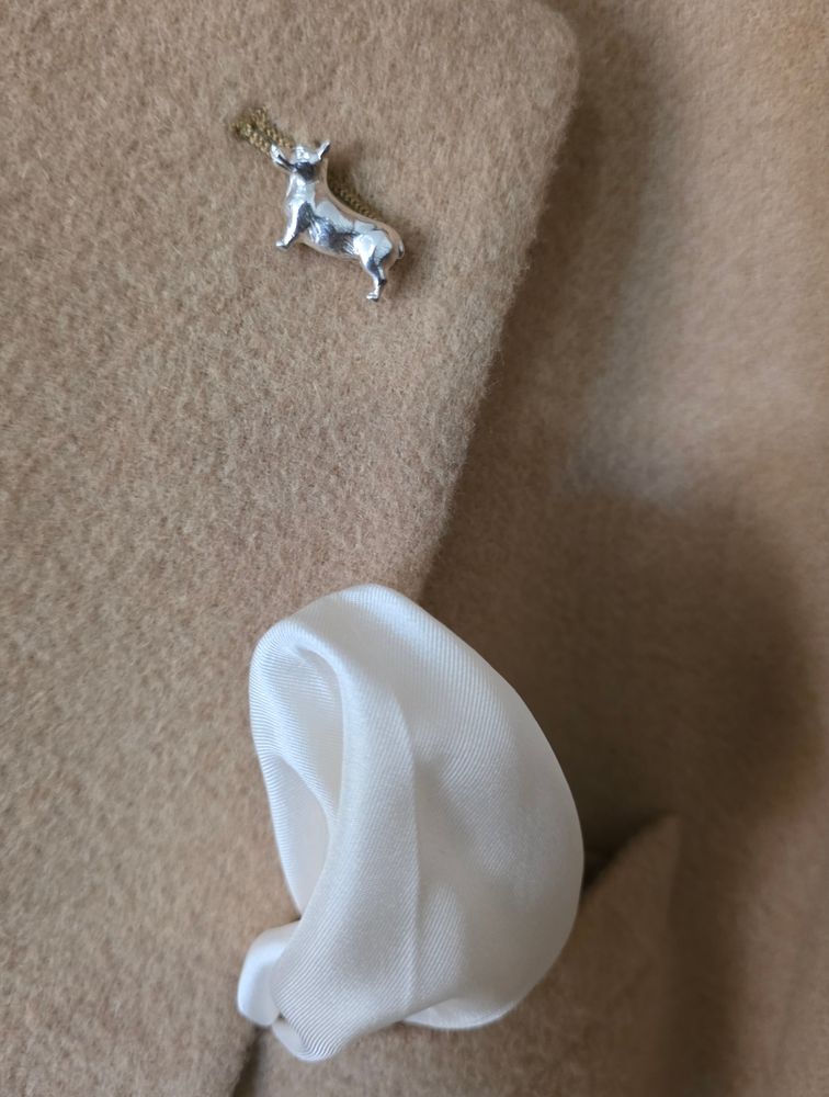 A silver corgi pin in the lapel of a camel hair jacket 