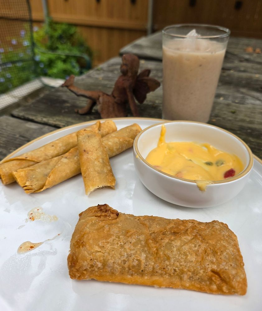 Three chicken flautas, queso, a mango pie, and a glass of horchata on the picnic table on the patio 