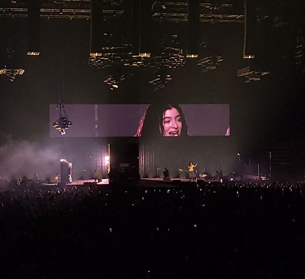 lorde on stage at a concert. the lights are mostly out, with soft warm lighting on the stage. 
