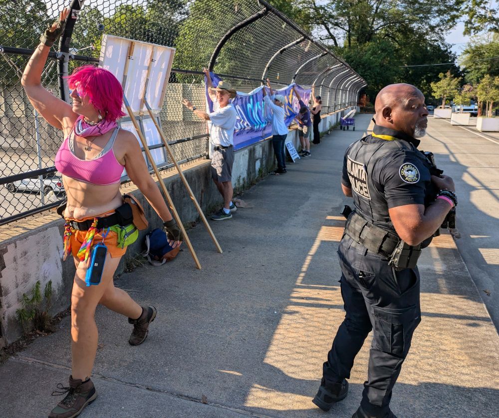A cop babysits us to ensure we un-affix our signs from the bridge fence.