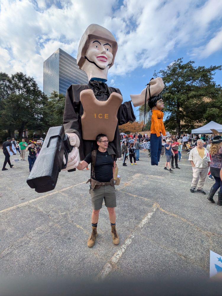 A man at at the no. Kings protest in Atlanta on October 18th, 2025 shoulders, a gigantic puppet of an ice agent holding a gun and a brown-skinned child by the scruff of the neck
