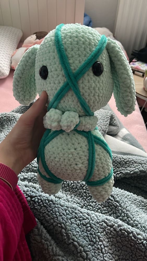 You see a crocheted rabbit in green that is tied with dark green wool