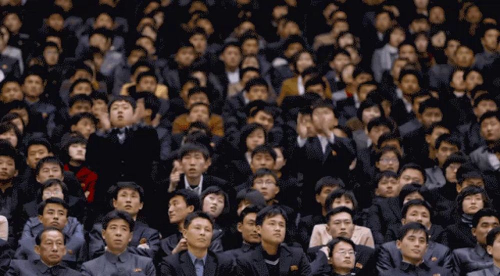 a large group of people are sitting in a stadium and one man has a red shirt on