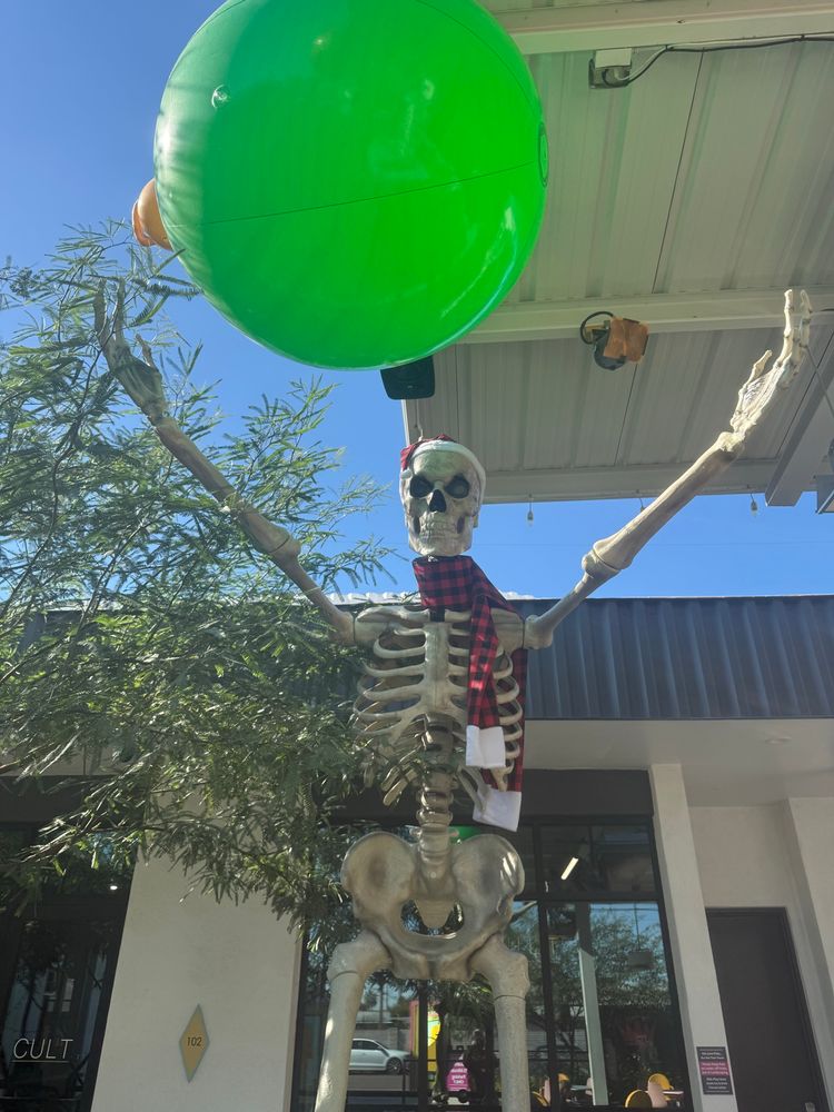 a 12 foot tall skeleton wearing a Santa Hat and scarf reaches for an oversized Christmas light