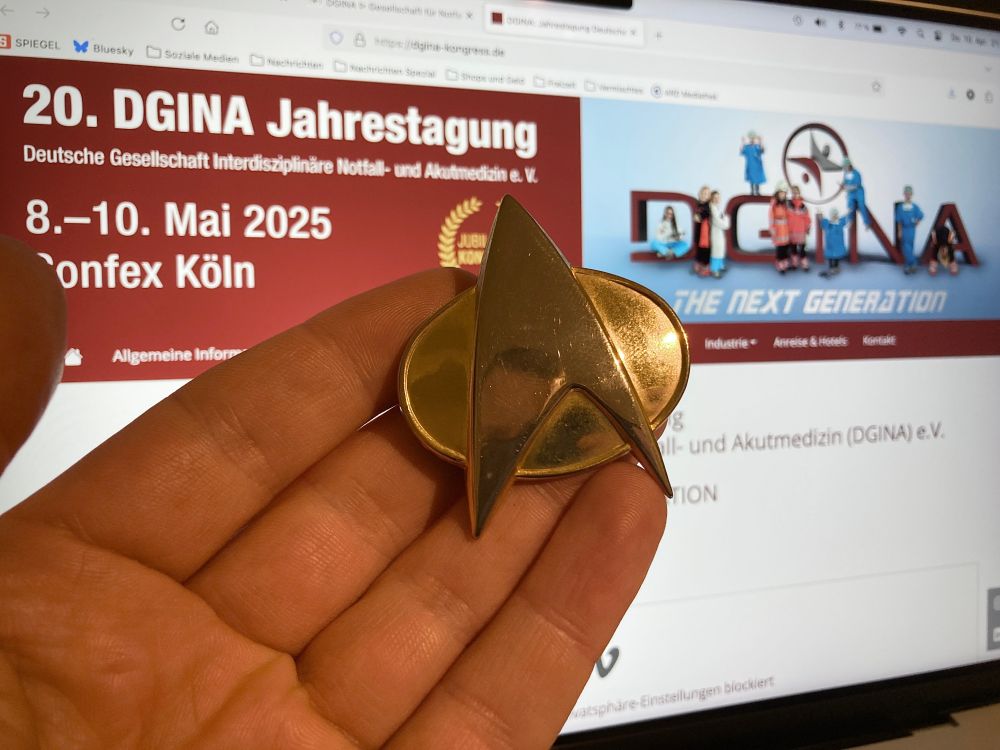 Website der 20. Jahrestagung der DGINA auf dem Bildschirm, davor eien Hand, die einen Anstecker von "Star Trek - The Next Generation" ins Bild hält