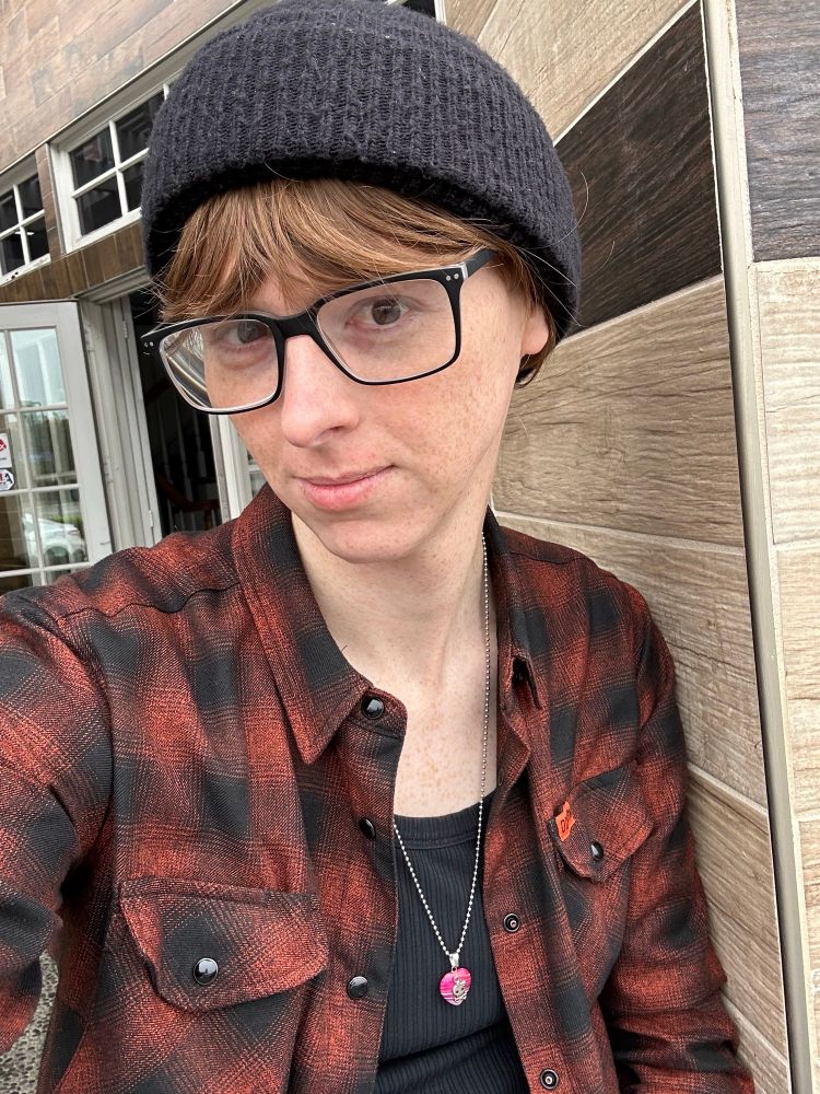 A girl in flannel, glasses, and a beanie without makeup