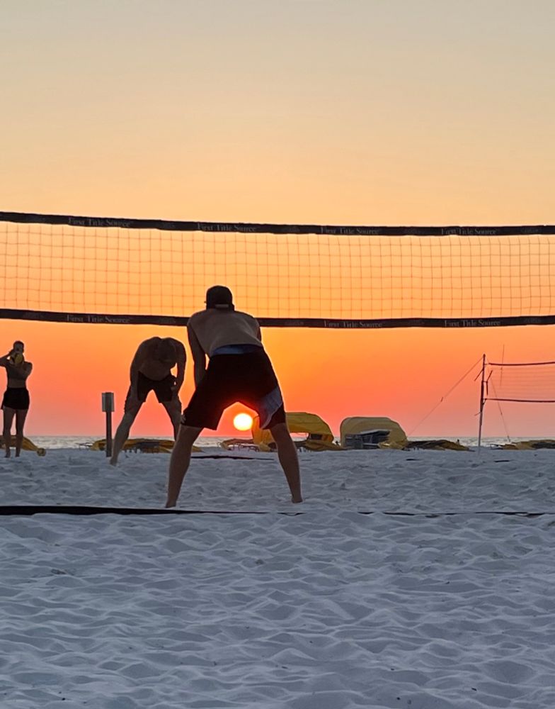 The sun setting between a young man’s legs as he plays volleyball on St. Pete’s Beach