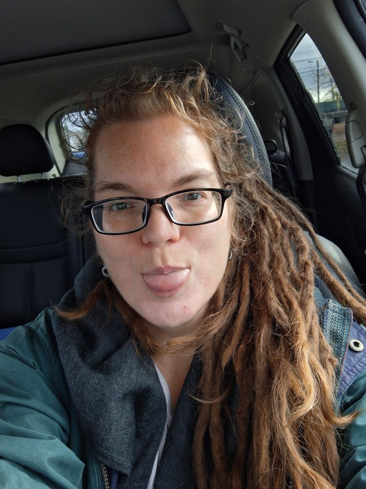 Me! White woman with black framed glasses and elflocks, sticking her tongue playfully at the camera