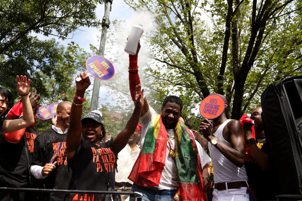 Jumaane Williams holds up a bottle of baby powder and squeezes to send up a cloud on the NYWFP float - folks around are cheering.