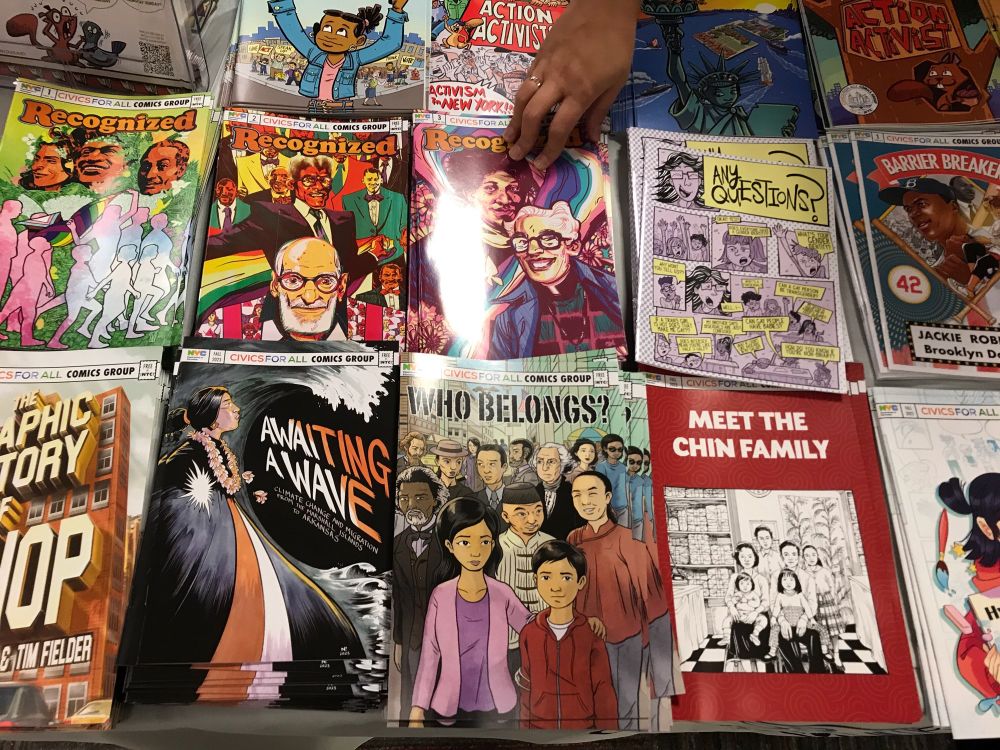Table of free NYC DOE educational comics at the NYCC including WHI BELINGS? AWAITING A WAVE, MERt the chin family, RECOGNIZED and many more