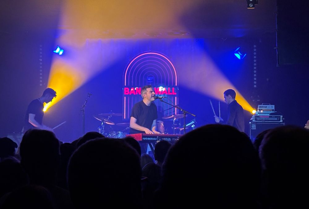 Band on stage blue and yellow lighting crowd in foreground 