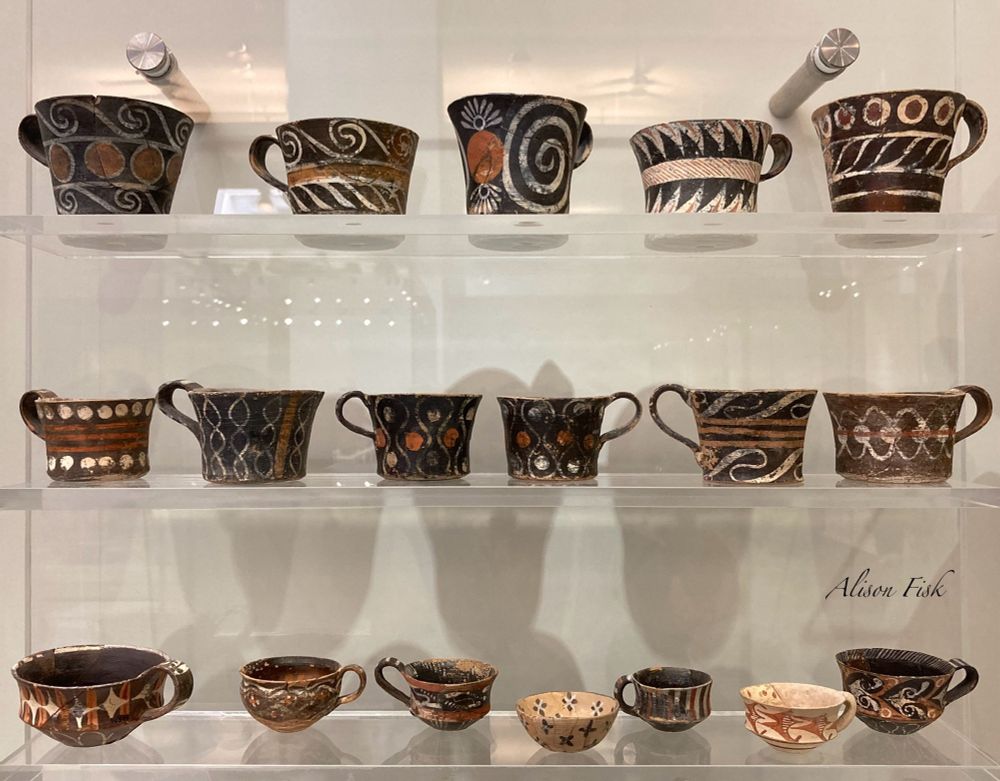 My photo shows a museum display with luxury Minoan ceramic cups known as Kamares Ware, from Phaistos, Crete. Produced by palace workshops c. 1800-1700 BC. The cups range in shape and size from conic and cylindrical cups (top and middle shelves) to hemispherical and carinated shaped cups (bottom shelf). They are decorated with multi-coloured geometric motifs. Many with spirals and swirls painted in red and white pigment on black.